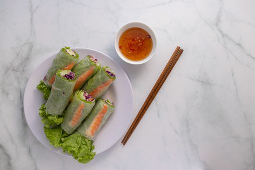 An overhead shot of Vietnamese spring rolls, fish sauce dip and chopsticks on a white table