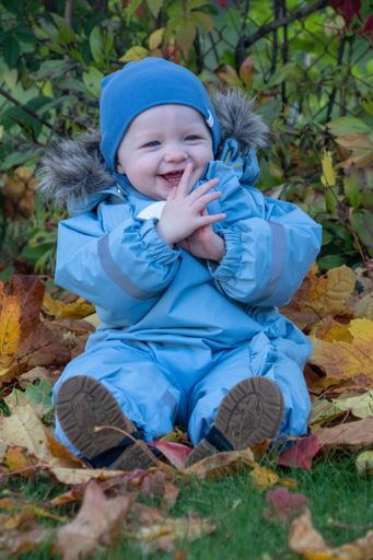 A happy caucasian Babyboy in winter blue outfit plays in the garden