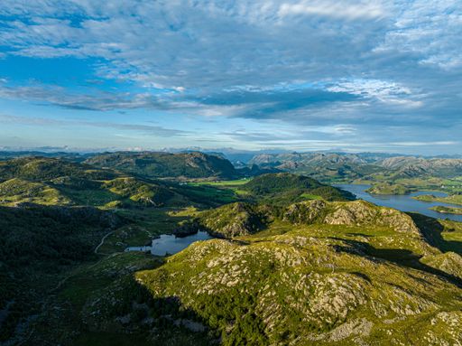 An aerial view of lakes among green mountains under blue cloudy sky in bright sunlight, Norway