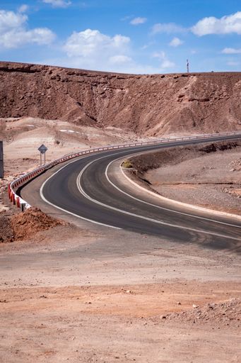 A vertical shot of an asphalt turning road in the Atacama Desert under mountains in Chile