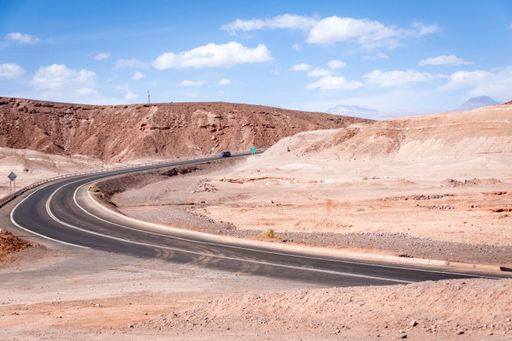An asphalt turning road in the Atacama Desert under mountains in Chile