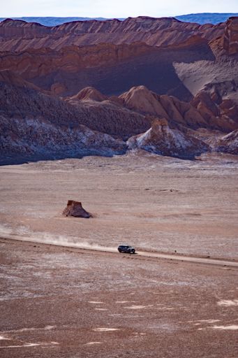 A vertical aerial shot of a car on a road between rocky mountains in the desert