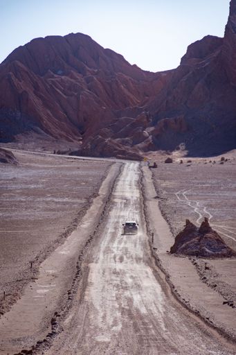 A vertical shot of a car on long road in the Atacama Desert under mountains in Chile