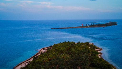 A done shot over Bahamas island with green land and lighthouse on the horizon under blue sky