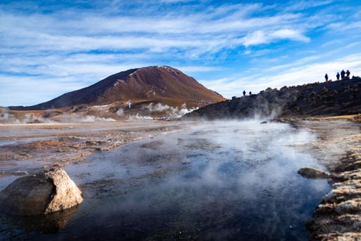 A landscape view of El Tatio Geyser with smoke over water under blue cloudy sky in Chile
