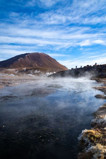 A vertical shot of the El Tatio Geyser with smoke over water under blue cloudy sky in Chile