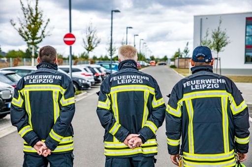 A closeup shot of three firefighters in a uniform with the writing "fire brigade of Leipzig" in German