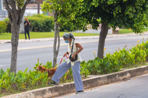 A lady in a mask crossing the road with her dog in Matanzas, Cuba