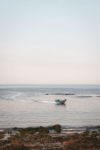 A vertical shot of a boat in the sea near a sandy beach under sunset sky