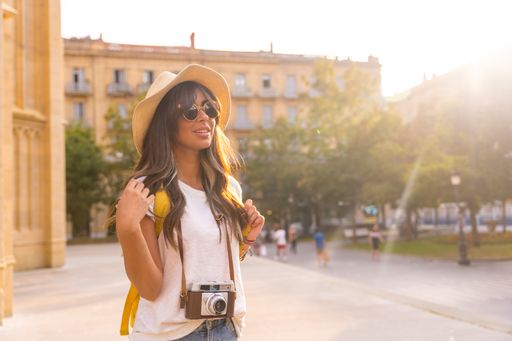 A young tourist female in a hat and sunglasses with a camera walking around and enjoying the view