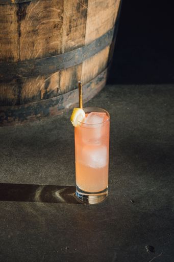 iced pink lemonade drink in tall glass on concrete floor next to whiskey bar