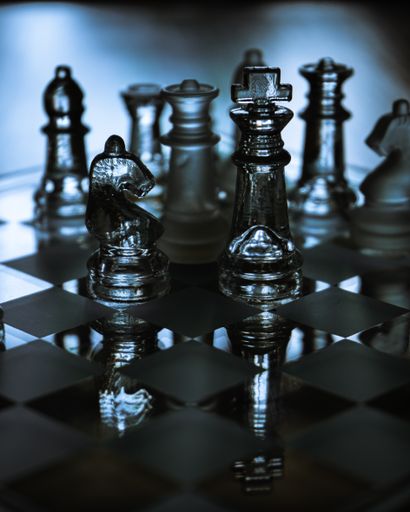 A selective focus shot of a glass chessboard in blue light - a concept of success, fighting and confronting problems