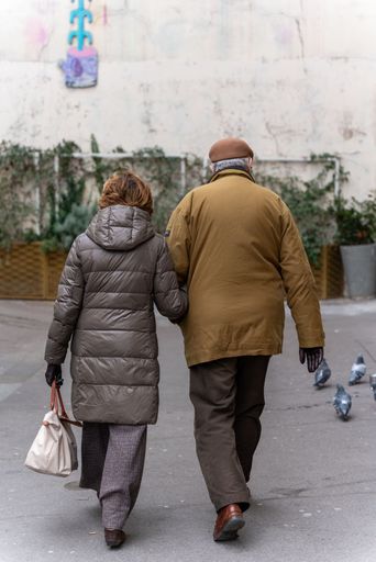 An elderly couple walks down a street while holding hands