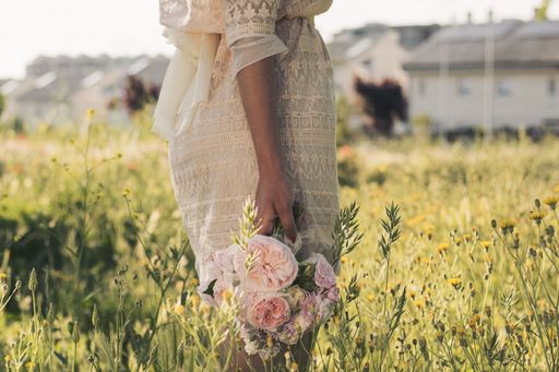 A closeup shot of a female in a white dress holding a bouquet of white and pink roses on a field