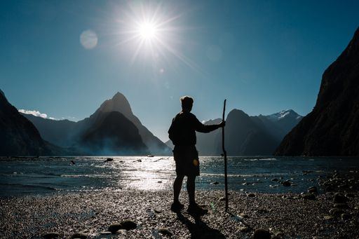A breathtaking shot of a male staring at the mountains on a sunny day in Milford Sound, New Zealand