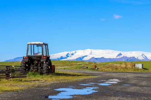 A tractor parked on the grass against a snow-covered mountain