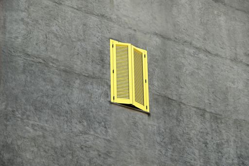 A single yellow-striped closed window on a rustic grey concrete wall.