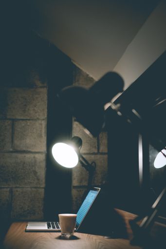 A vertical shot of a glass of coffee next to a laptop with study lamps