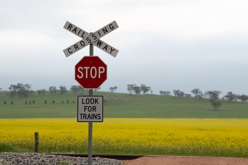 A sign that says 'Crossing Railway Stop Look for trains' posted on the side of the tracks with a beautiful meadow on the background