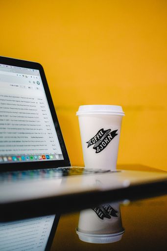 A vertical shot of a take away coffee next to a laptop
