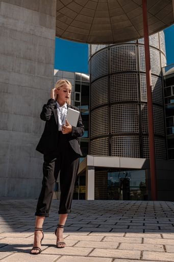 A vertical shot of a young blonde business lady posing in front of a building