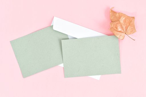 A top view of grey invitation cards placed on a pink surface next to pink flowers