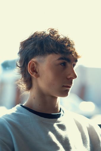A vertical portrait of a young Caucasian boy with a fresh mullet haircut