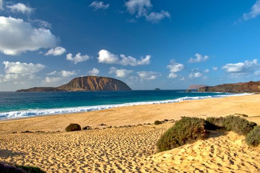 An idyllic sandy beach with mountains and a cloudy sky in the background