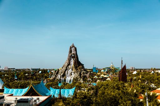 A vibrant amusement park surrounded by lush green trees and a clear blue sky: volcano bay Orlando