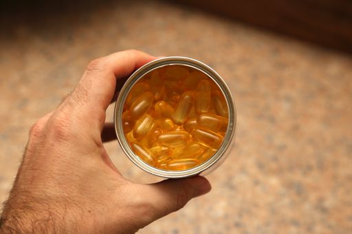 A top view shot of a can full of fish oil capsules being held by a person's hand