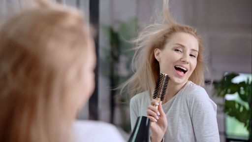 A young blonde female having fun in the mirror while using a blowdryer to style her hair