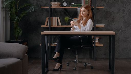 A Caucasian red-haired woman typing on her phone while sitting in an office.