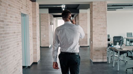 A Caucasian man on a call while walking in a corridor. Pictured from the back.