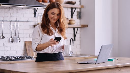 A Caucasian businesswoman looking at her phone in a kitchen