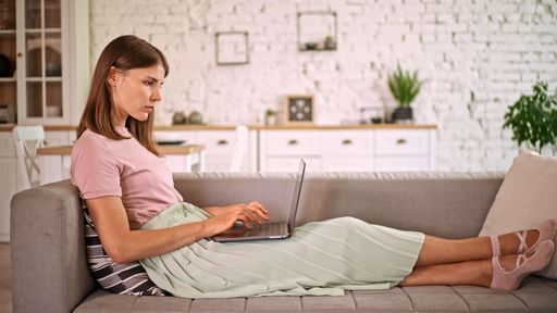 A Caucasian business woman lying on a sofa and working on laptop