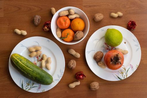 A top view of plates on a wooden table with different fruits, nuts and cucumber