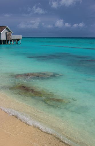 A vertical shot of a small beach house on the shore with a blue cloudy sky in the background, Maldives