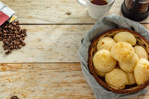 many cheese breads or 'pao de queijo' in basket and french press coffee maker and coffee beans, with fabric around over table with copy space