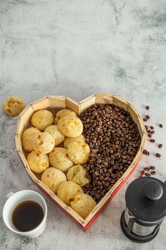 brazilian cheese bread or 'pao de queijo' in a heart shaped format basket, with coffee beans on a marble or stone surface