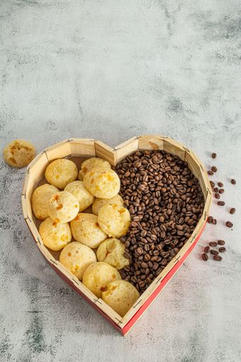 brazilian cheese bread or cheese bun in a heart shaped format basket, with coffee beans on a marble or stone surface
