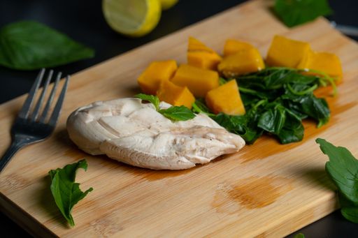 A closeup of sliced pumpkin with chicken meat and herbs on the chopping board.