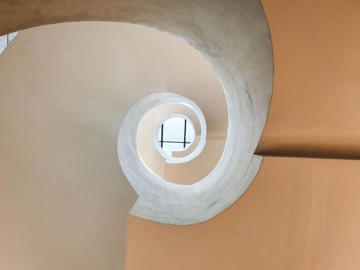 A low angle shot of a spiral concrete staircase with a window at the top