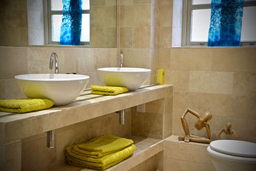 A modern bathroom with two sinks yellow towels and a toilet