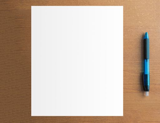 An overhead shot of a blank paper next to a pen on a wooden surface