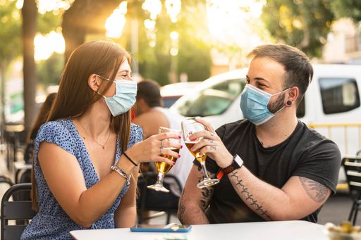 A shallow focus shot of a Caucasian couple with face masks having fun in an outdoor cafe - concept of the new normal