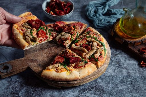 A close-up shot of a man's hand picking up a slice of a vegan tofu pizza on a rustic table
