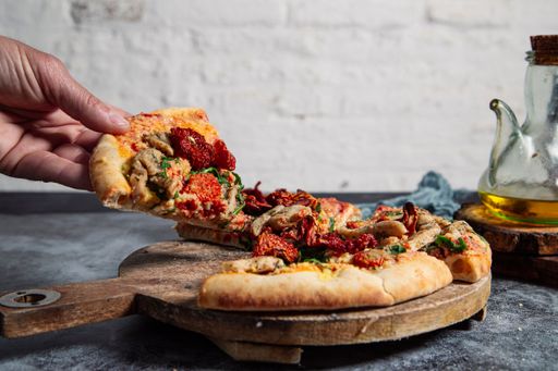 A close-up shot of men's hands picking up a slice of a vegan tofu pizza on a rustic table