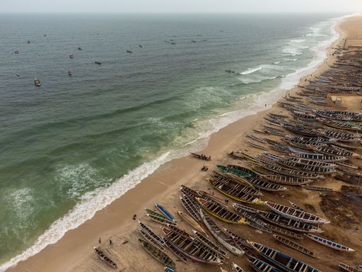Aerial seascape with the shore dividing diagonally the scene. One side contains yhe ocean with boats sailing, and the other with the beach
