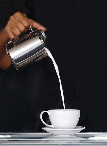 The milk being poured in the white cup by someone