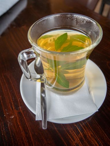 Vertical closeup shot of healthy aromatic tea with fresh mint in transparent glass cup on dark wooden table